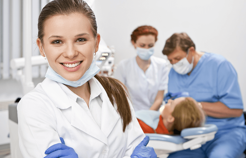 female dentist standing in front of a patient with two other dentists in background