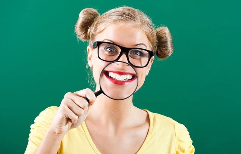 young blonde female with glasses and magnifying glass over smile