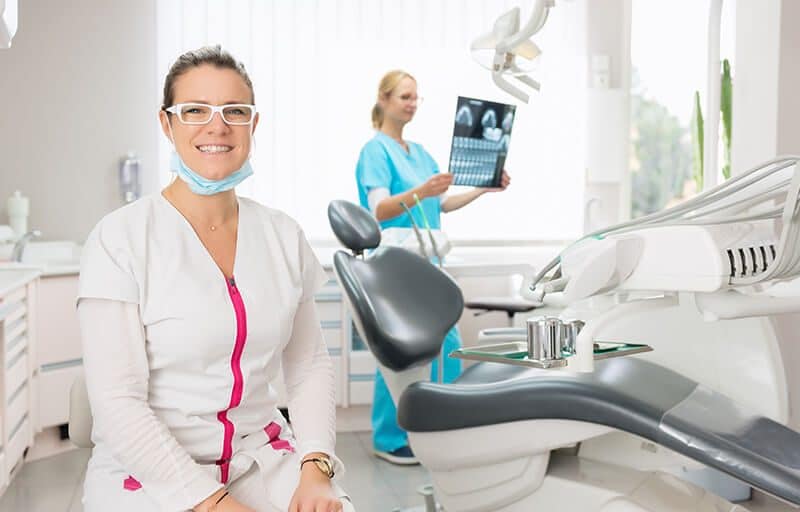 female dentist smiling with another female dentist examining x-ray in background